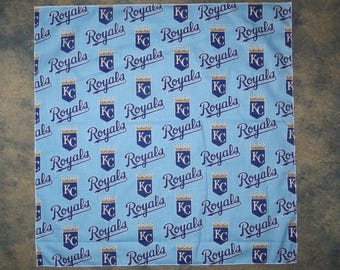 May include: A light blue bandana with a repeated pattern of the words "Royals" and "KC" in a navy blue script font. The "KC" is stylized with a crown above the letters.