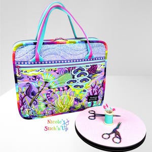 May include: A colorful tote bag with a zipper closure, featuring a vibrant underwater scene with seahorses and coral. The bag has a matching handle and a small pink round mat with sewing tools.