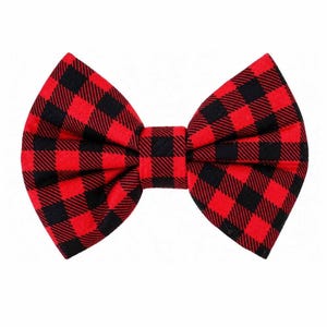 May include: A red and black buffalo plaid bow tie. The bow tie is made of fabric and features a classic checkered pattern. The bow tie is a stylish accessory for formal or casual wear.