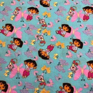 May include: A light blue fabric with a repeating pattern of a cartoon girl, a monkey, and butterflies. The girl is in a pink outfit and the monkey is red. The butterflies are pink, purple, and yellow.