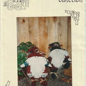 May include: Two handmade woodland elves with white beards and red hats. The elves are sitting on a bed of brown moss in front of a wooden wall. The image is titled "Woodland Elves" and the text "Ginger Snap Junction" is at the top of the image.