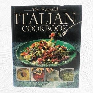 Op de afbeelding: De omslag van het kookboek "The Essential Italian Cookbook" toont een foto van pasta met tomatensaus en groene groenten op een groen bord. De omslag bevat ook vier kleinere foto's van kookstappen. De tekst op de omslag luidt "The Essential Italian Cookbook" en "50 Classic Recipes, With Step-by-Step Photographs Edited by Heather Thomas."