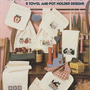May include: A collection of eight cross-stitch patterns for kitchen towels and pot holders. The patterns feature a variety of designs, including apples, cats, and hearts. The designs are printed on a white background with black text. The text reads "Kitchen Mates 8 Towel and Pot Holder Designs".
