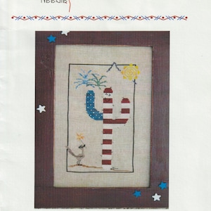 May include: Cross stitch pattern for a July calendar cactus with a red, white, and blue design. The cactus is wearing a red, white, and blue hat and has a red, white, and blue design on its body. The cactus is surrounded by stars and a sun. The text "July Calendar Cactus" is at the bottom of the image.