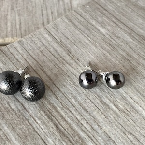 Puede incluir: Dos pares de pendientes de botón negros. Un par es brillante y el otro par tiene un acabado texturizado.