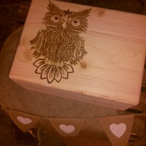 Peut inclure: Une boîte en bois avec un motif de hibou brûlé au bois. Le hibou est brun et a un design détaillé. La boîte est posée sur une surface en toile de jute avec des cœurs blancs.