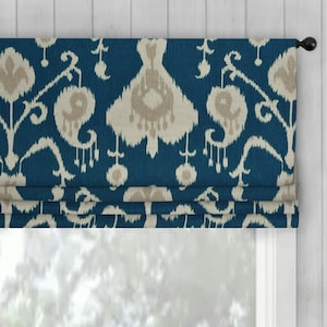 May include: A blue and beige patterned window valance. The valance has a repeating ikat design in beige against a deep blue background. The valance is mounted on a black rod and is above a window with a white frame.