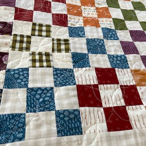 May include: A patchwork quilt with a variety of fabrics in shades of blue, green, red, and brown. The quilt is made up of squares and rectangles, and the fabric patterns include plaid, floral, and geometric designs.