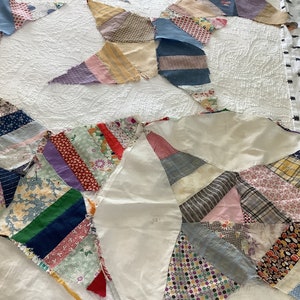 May include: A handmade quilt in a starburst pattern, featuring various fabric scraps in a range of colors and patterns. The quilt is laid out on a white bedspread, showcasing the intricate patchwork design and the textures of the fabrics.