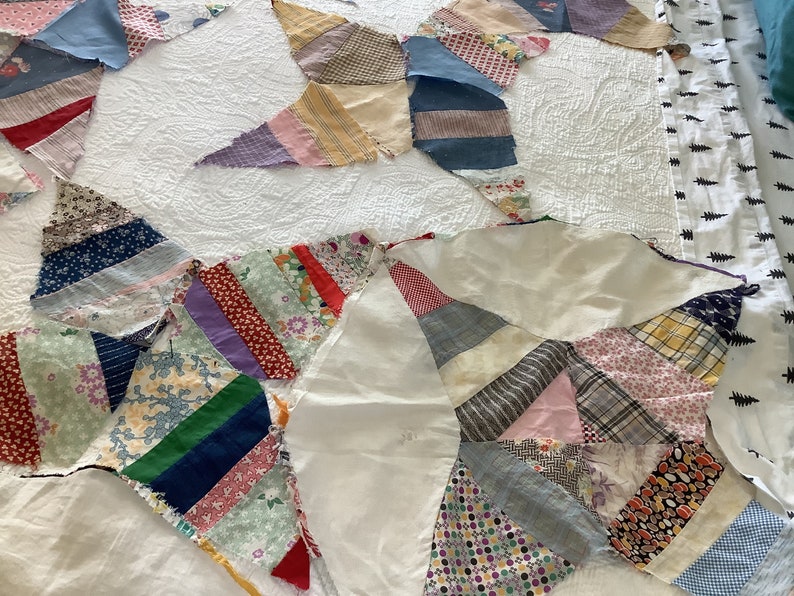 May include: A handmade quilt in a starburst pattern, featuring various fabric scraps in a range of colors and patterns. The quilt is laid out on a white bedspread, showcasing the intricate patchwork design and the textures of the fabrics.