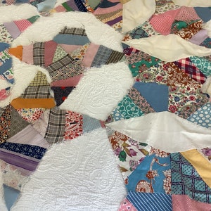 May include: A patchwork quilt with a white background and colorful fabric patches. The patches are various shapes and sizes, featuring floral, plaid, and patterned designs in shades of blue, pink, green, and yellow. The quilt has a quilted texture.