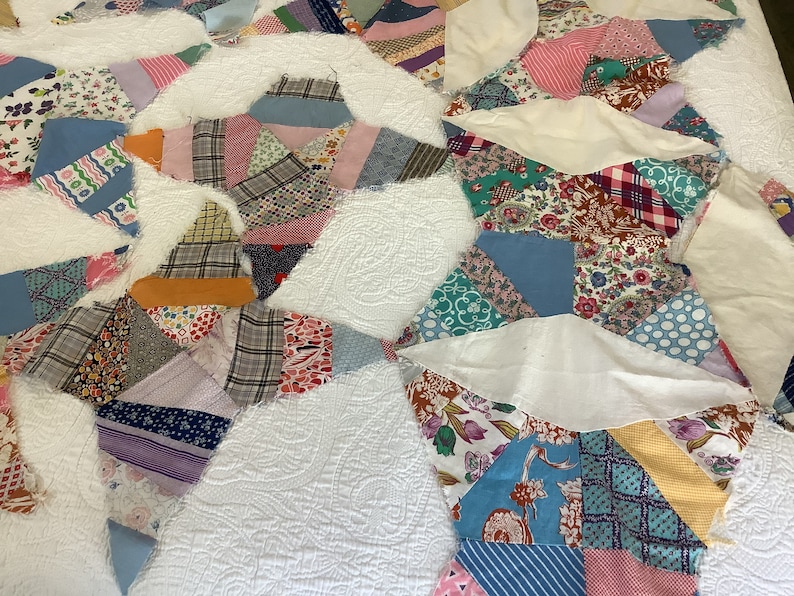 May include: A patchwork quilt with a white background and colorful fabric patches. The patches are various shapes and sizes, featuring floral, plaid, and patterned designs in shades of blue, pink, green, and yellow. The quilt has a quilted texture.