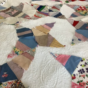 May include: A handmade quilt with a starburst design. The quilt features a white background with a quilted pattern and colorful patchwork pieces in various patterns and colors, including blue, pink, and floral prints.