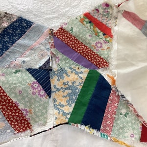 May include: Close-up of a handmade quilt with a starburst design. The quilt features various fabric patterns in shades of blue, red, green, and purple. The quilt is made of small fabric pieces sewn together, creating a unique and colorful textile.