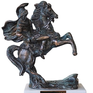 May include: Bronze sculpture of a warrior on horseback rearing up. The warrior wears a helmet and cape. The sculpture is mounted on a white marble base with gold lettering that reads "ΑΛΕΞΑΝΔΡΟΣ THE GREAT 330BC".