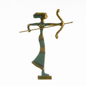May include: A bronze-toned statue of a woman with a bow and arrow. The figure is in a shooting pose, with a long dress and a headdress. The statue has a teal and gold color scheme and is mounted on a rectangular base.