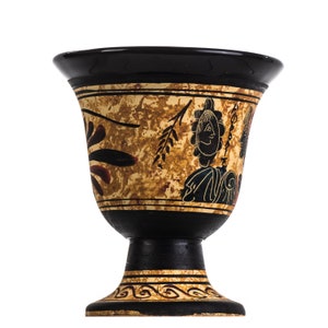 May include: A black and gold ceramic goblet with a pedestal base. The goblet features a painted design of a figure and foliage. The rim and base are black, with gold accents and a textured background.