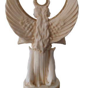 May include: White marble statue of a two-faced goddess with wings and a crescent moon on her head. The goddess is holding two white cats in her arms. The statue is on a round base with a gold inscription.