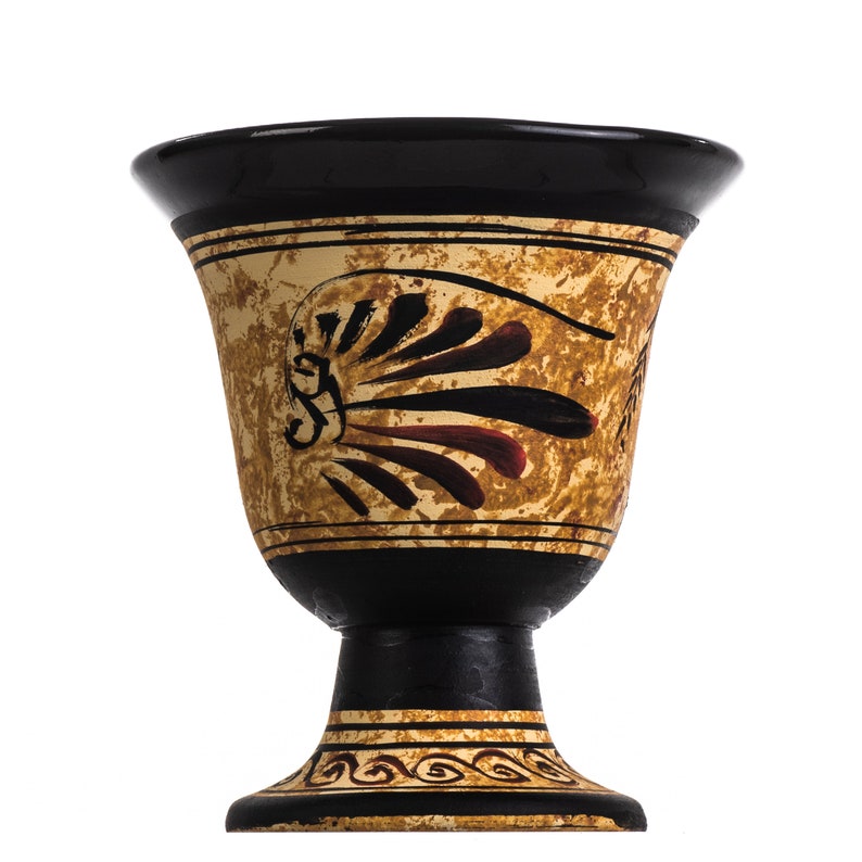 May include: A black and gold ceramic chalice with a pedestal base. The chalice features a textured gold surface with black and red painted details. The rim and base are black with gold trim. The design is reminiscent of ancient Greek pottery.