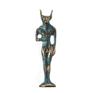 Op de afbeelding: Een bronzen sculptuur van een mensachtige figuur met stierhoorns en een menselijk gezicht. De figuur heeft een blauwgroene patina en gouden accenten, met een ontbrekende arm en een gat in de torso. De sculptuur staat op een ronde basis.