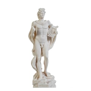以下が含まれることがあります： ギリシャ神アポロンの白い大理石の像で、リュートを持ち、ゆったりとしたローブを着ています。像は「APOLLON」と刻まれた台座の上に立っています。