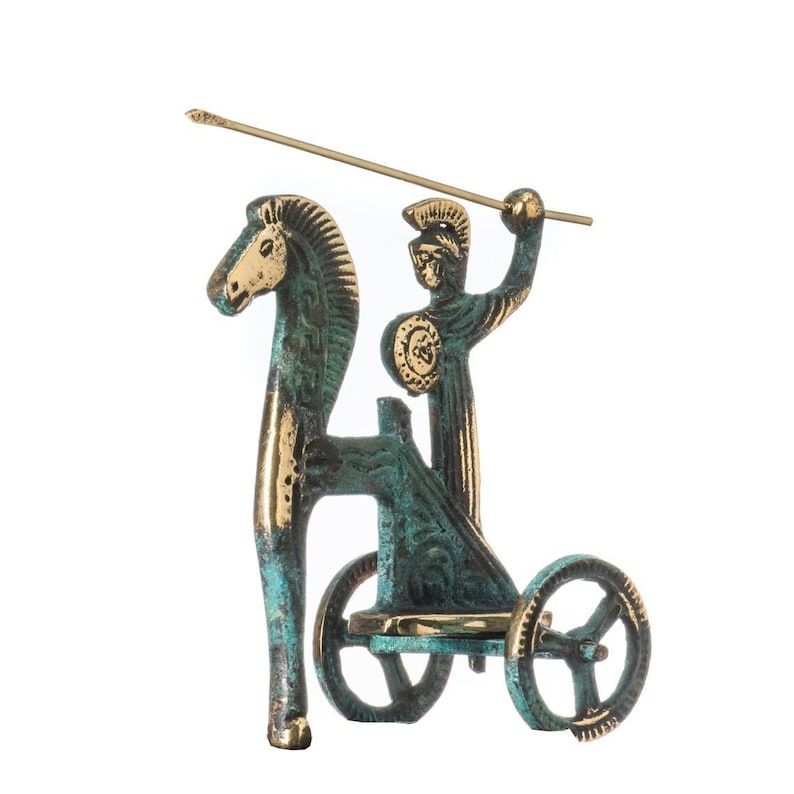 May include: A bronze-colored statue depicting a figure in a chariot pulled by a horse. The figure is holding a spear. The statue has a weathered, aged appearance with hints of teal and gold.