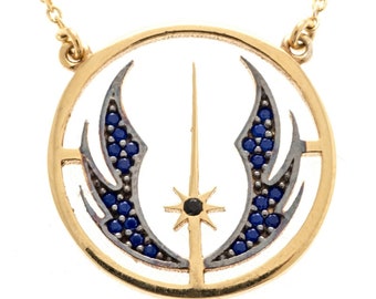 May include: A gold necklace with a pendant featuring the Rebel Alliance symbol. The symbol is made of gold and has blue gemstones around the edges. The pendant is round and has a black gemstone in the center.