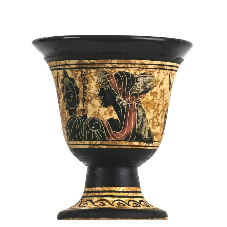 May include: A black and gold ceramic chalice with a pedestal base. The chalice features a painted scene of a woman in profile with red and black accents. The rim and base are black, with gold decorative bands.