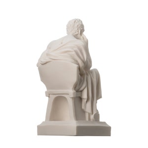 May include: White marble statue of a seated figure, the figure is draped in a toga and is looking down. The statue is on a rectangular base.
