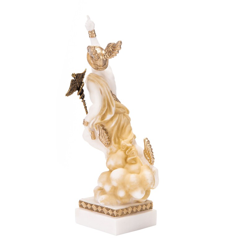 Puede incluir: Estatua de m&aacute;rmol blanco de una figura alada con detalles dorados, de pie sobre una base en forma de nube. La figura sostiene un bast&oacute;n con una parte superior alada.