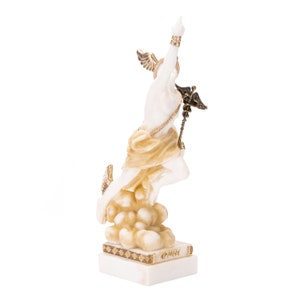 Puede incluir: Estatua de m&aacute;rmol blanco de la diosa griega Nike, con detalles dorados, de pie sobre una base de nube. La estatua est&aacute; sobre una base de m&aacute;rmol blanco con la palabra "&Epsilon;&Rho;&Mu;&Eta;&Sigma;" inscrita en ella.