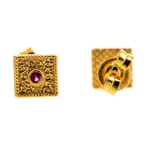 May include: A pair of gold square stud earrings with a small pink gemstone in the center of each earring.
