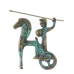 May include: A bronze-toned figurine depicting a chariot pulled by a horse, with a warrior figure holding a spear and shield. The figurine has a weathered, antique appearance, with green and gold accents. The spear extends horizontally.