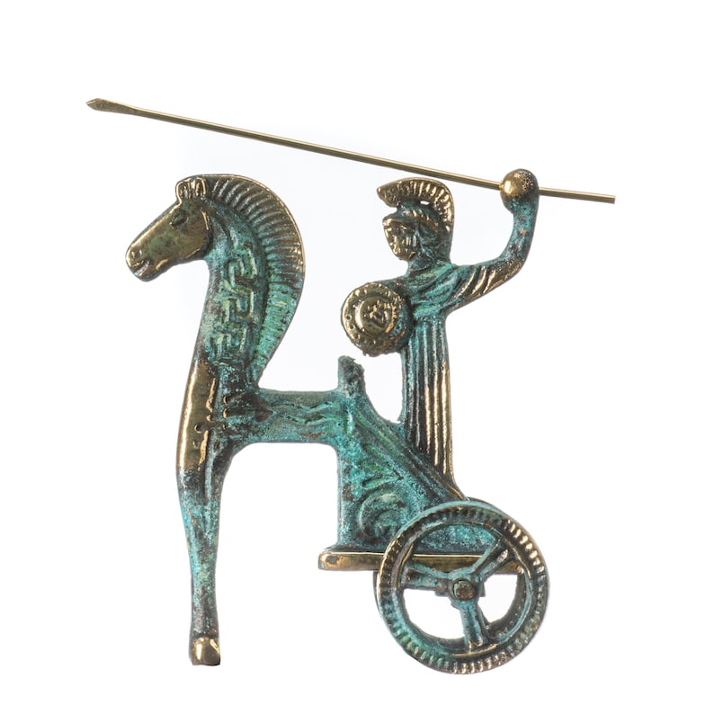 May include: A bronze-toned figurine depicting a chariot pulled by a horse, with a warrior figure holding a spear and shield. The figurine has a weathered, antique appearance, with green and gold accents. The spear extends horizontally.