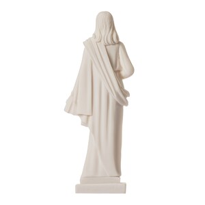 May include: White marble statue of a person wearing a long robe, standing on a square base. The statue is facing away from the camera.