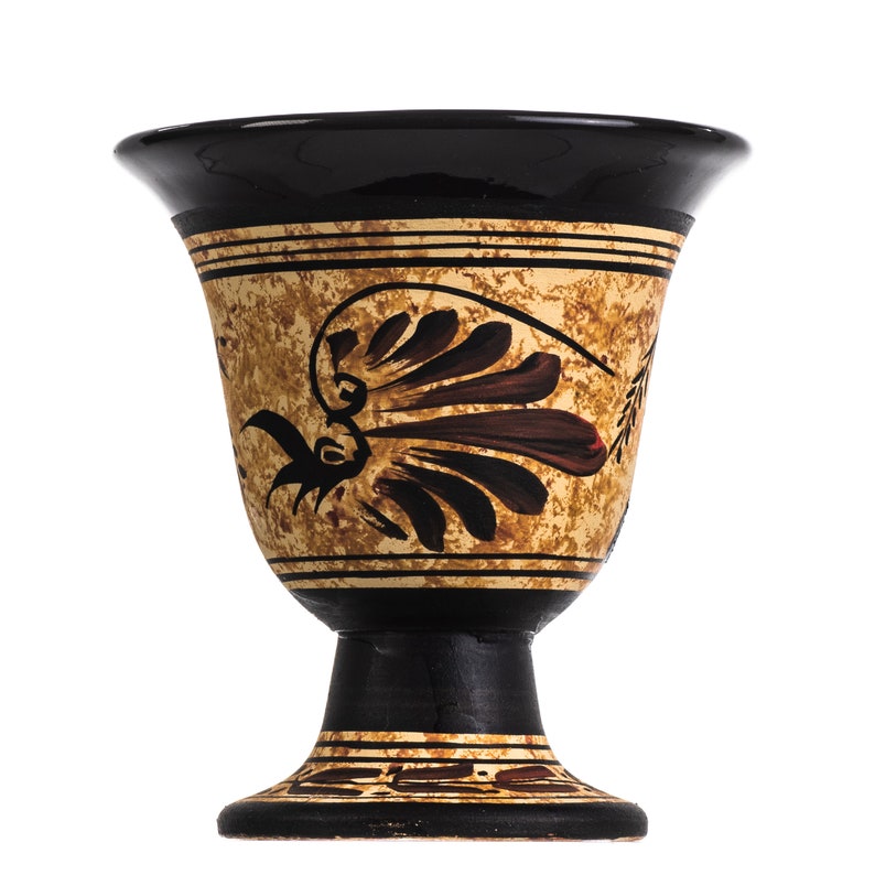 May include: A black and brown ceramic goblet with a decorative design of a stylized bird and a fan-shaped motif. The goblet has a wide, round base and a narrow, cylindrical stem.