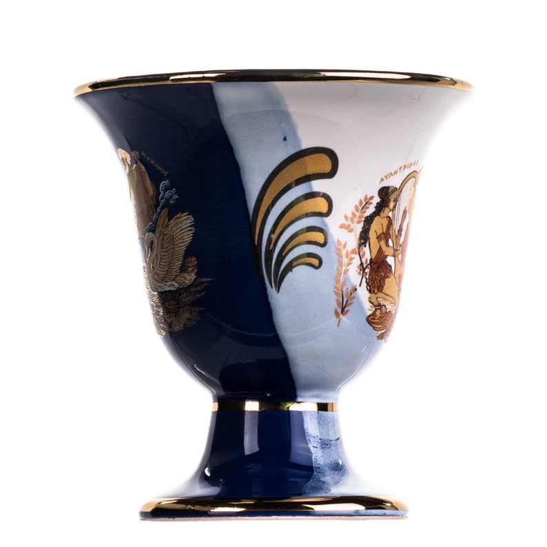 May include: A blue and white ceramic goblet with gold accents and a painted design of a woman playing a lyre and a swan. The goblet has a wide, round bowl and a tall, slender stem.