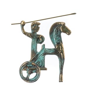 May include: A bronze-colored decorative chariot figurine with a figure holding a spear and riding a horse. The chariot has a single wheel and the horse has decorative markings on its neck. The figurine has a patina finish.