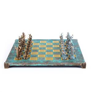 Peut inclure: Un jeu d'échecs composé d'un plateau carré à la finition bleu sarcelle et or patinée. Le plateau présente des coins décoratifs. Un côté comporte des pièces de couleur bronze, tandis que l'autre côté présente des pièces argentées, alignées.