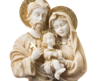 May include: A white ceramic sculpture of the Holy Family.  The sculpture depicts Joseph, Mary, and baby Jesus.  Joseph is holding a cross and Mary is holding Jesus.  The sculpture has gold accents.