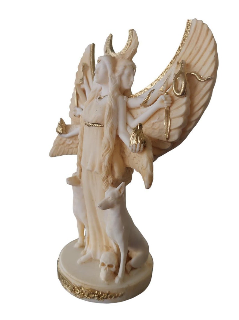 May include: A white and gold statue of a three-headed goddess with wings, holding a snake, a torch, and a crescent moon. The goddess is standing on a base with two dogs and a skull.