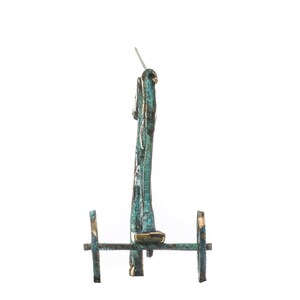 May include: A bronze-colored, miniature chariot with two wheels and a vertical structure. The chariot has a patina finish with hints of teal and gold. A small, silver-colored pin extends from the top.