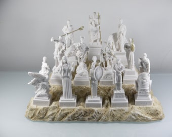 May include: A white marble set of 15 Greek god and goddess figurines on a stone base. The figurines are arranged in a tiered display, with the largest figurine at the top and the smallest figurines at the bottom.