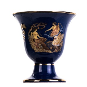 May include: A blue ceramic vase with a gold rim and a gold design of a swan, a woman, and a man. The vase has a wide mouth and a round base.