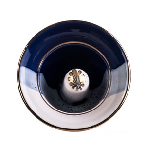 May include: A blue and white ceramic ring holder with a gold rim and a gold floral design. The holder is empty and ready to display a ring.