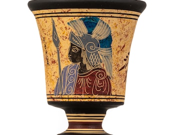 May include: A ceramic goblet with a black rim and base. The goblet is decorated with a yellow, red, and blue image of a warrior wearing a helmet and holding a spear. The warrior is depicted in a black silhouette against a yellow background.