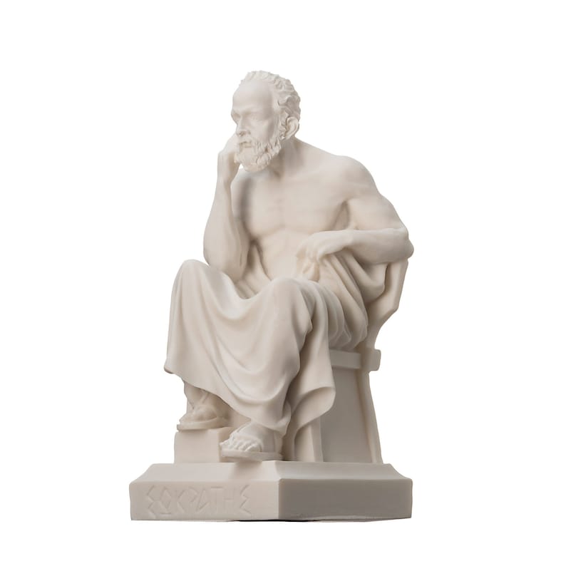 May include: White marble statue of a seated man with a beard, wearing a toga. The statue is on a square base with the word "SOCRATES" inscribed on it.