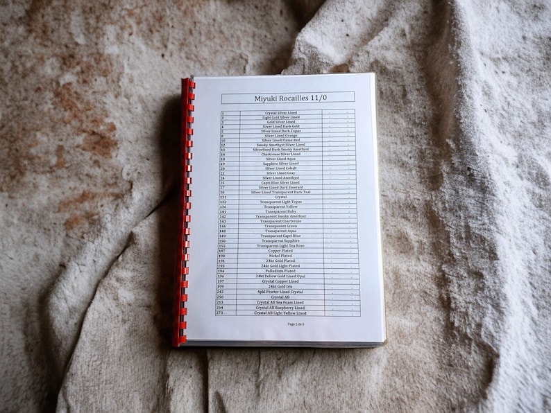 May include: A white, spiral-bound book with the title "Miyuki Rocailles 11/0" printed on the cover. The book lists different colors of beads with corresponding numbers.