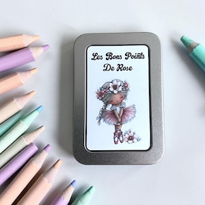 Peut inclure: Une boîte rectangulaire en métal argenté avec une étiquette blanche portant le texte Les Bons Points De Rose et une illustration d'un personnage portant une couronne de fleurs et un tutu rose, entourée de plusieurs crayons en bois pastel.