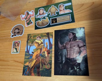 May include: A collection of fantasy-themed art prints and stickers featuring muscular characters in forest settings. The items include a sticker sheet with the text UNLEASH THE BEAST, a small rectangular card, and two larger rectangular prints depicting figures.